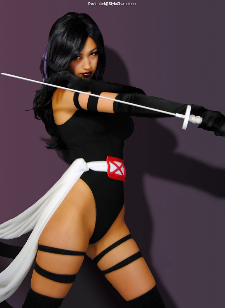 A female character in a black bodysuit wielding a sword, posing confidently with one arm extended. She has long dark hair and is accessorized with gloves and a belt featuring a distinctive emblem.