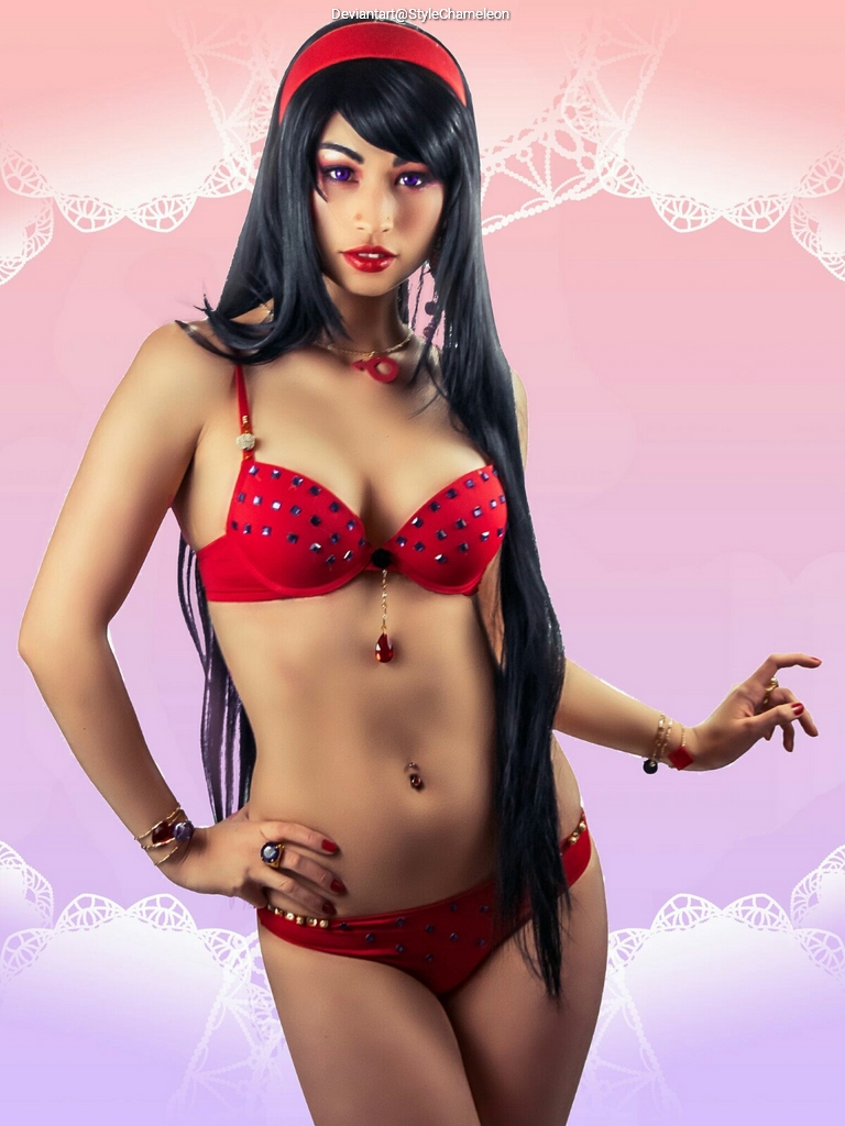 A woman in a red bikini with decorative elements poses confidently in front of a soft pink background. She has long black hair and bold makeup, accessorized with jewelry.