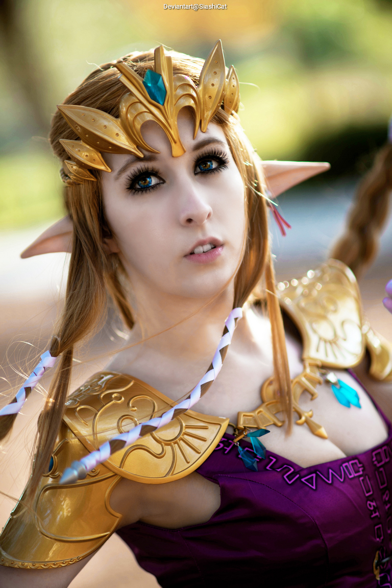 Close-up portrait of a woman in an elaborate fantasy costume with a golden crown and armor, featuring long braided hair and striking blue eyes.