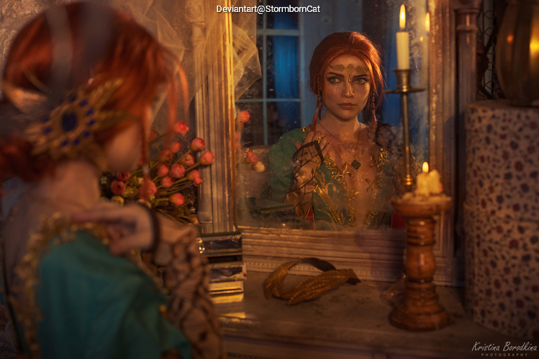 A woman with red hair and elaborate costume gazes into a mirror, surrounded by candles and flowers, creating a serene and mystical atmosphere.