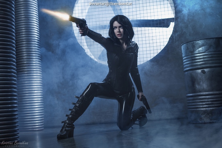 A woman in a black leather outfit is kneeling and aiming a handgun in a dramatic pose, with smoke and industrial elements in the background.