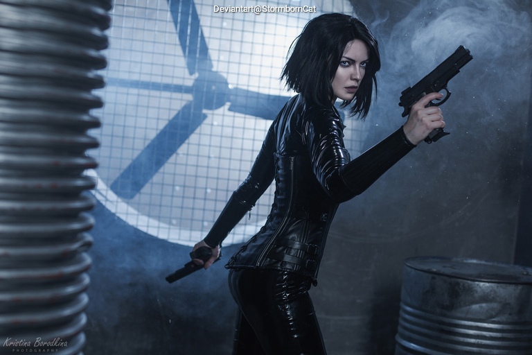 A skilled female figure in a black, form-fitting outfit poses dramatically with two guns in a moody, industrial setting, featuring a large fan in the background.