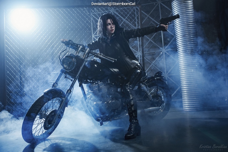 A person in a black outfit and leather jacket is posed on a motorcycle, pointing a gun while surrounded by smoke and dramatic lighting.