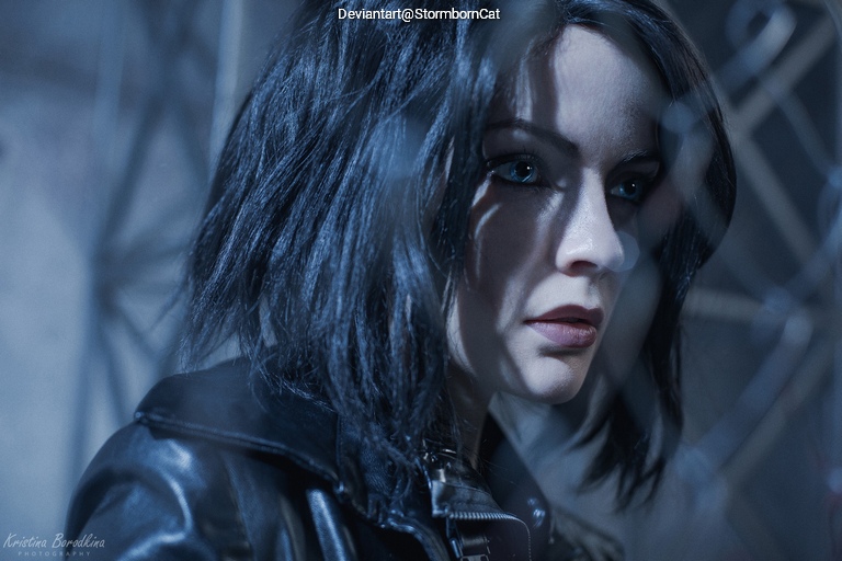Close-up of a person with short dark hair wearing a leather jacket, captured in a dimly lit environment with soft shadows and focus on facial features.