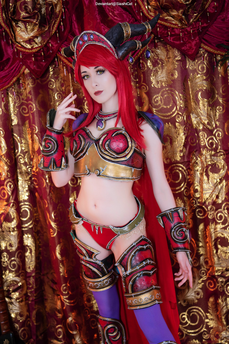 A model in an elaborate red and gold costume with horned headpiece, posing against a rich, decorative background.