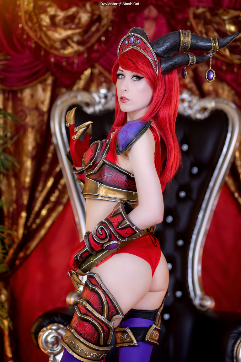 A cosplayer with bright red hair and intricate armor poses confidently in front of a lavish backdrop.