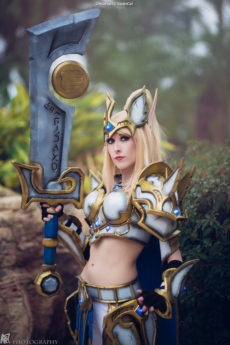 A person posing in a fantasy-themed costume with ornate armor and a large sword, featuring intricate designs and blue accents.