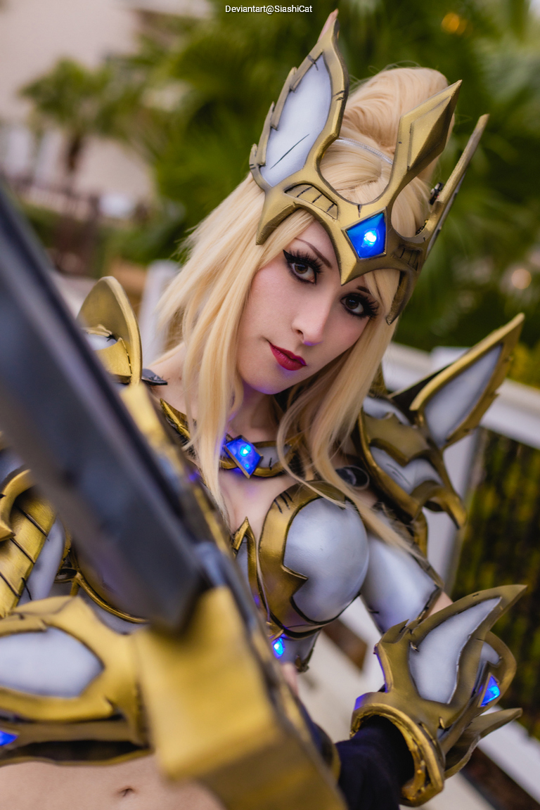 A person dressed in elaborate golden and silver armor with glowing blue accents, styled as a fantasy character. The photo captures a close-up of their face, showcasing striking makeup and long blonde hair.