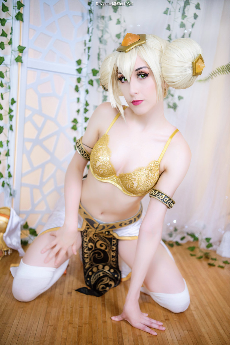 A person in a golden elaborate costume poses in a kneeling position with a decorative background.