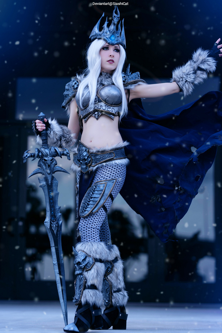 A person dressed in a fantasy costume resembling a character with a crown, metallic armor, and a long cape, holding a large weapon, surrounded by a snowy atmosphere.
