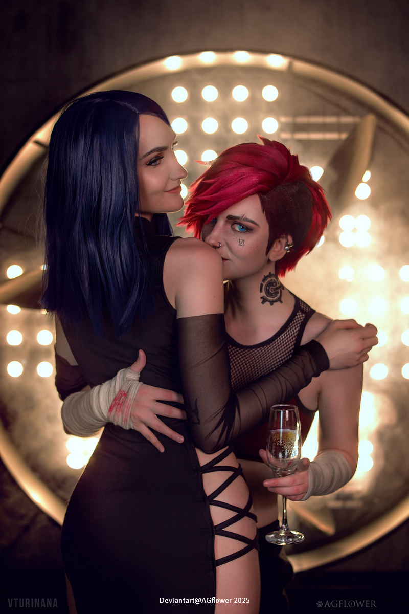 Two individuals in stylish outfits pose closely together, with one wearing a black dress and the other in a top with a playful expression. The background features bright circular lights, creating a dramatic atmosphere.