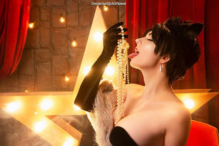Model in a black outfit with cat ears, playfully holding and licking a string of pearls in a glamorous, theatrical setting with soft lighting and a star backdrop.