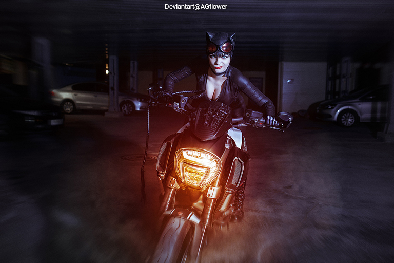 A woman dressed as a cat-like character poses on a motorcycle in a dimly lit parking garage, exuding a confident and adventurous vibe.