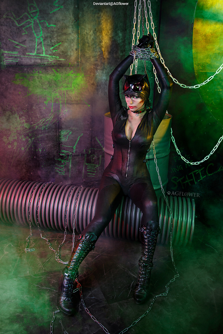 A person dressed in a black cat costume with chains, posing in a dark, colorful environment with mist and graffiti on the walls.