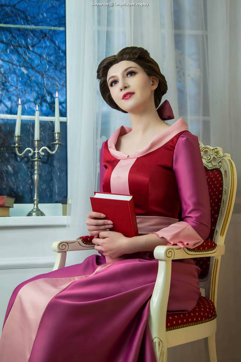 A woman in a burgundy and pink dress seated in an ornate chair, holding a red book, with candles and a window showing a dark landscape in the background.