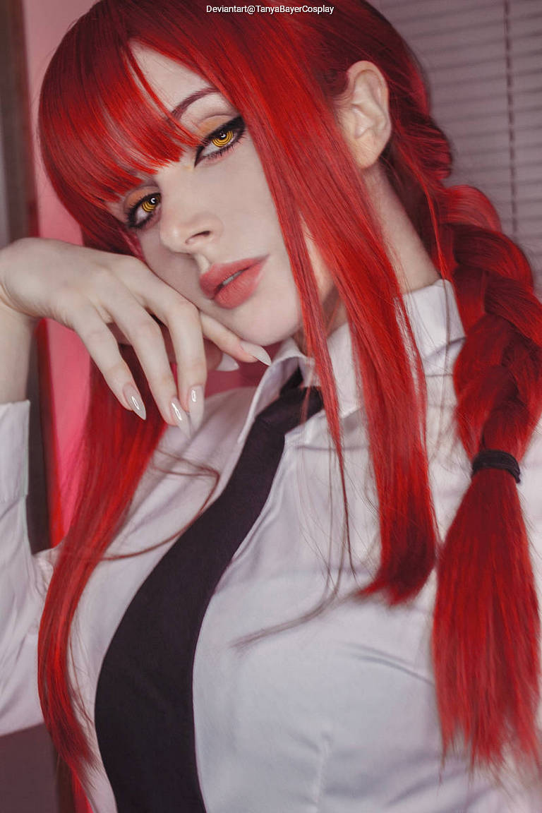A close-up portrait of a person with vibrant red hair styled in braids, wearing a white shirt and black tie, with striking yellow eyes and a thoughtful expression.