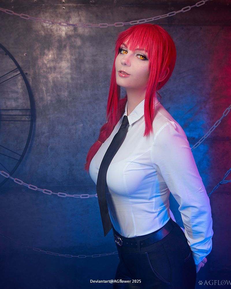 A person with bright red hair and yellow eyes poses confidently, wearing a white shirt and a black tie, against a backdrop of chains and blue lighting.