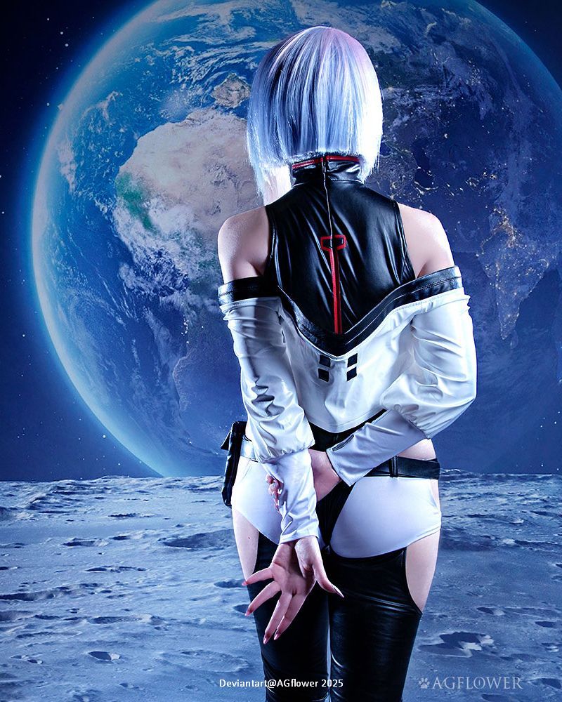 A figure with short, light blue hair wearing a futuristic outfit stands with their back to the camera, facing a large Earth in space, against a starry background.