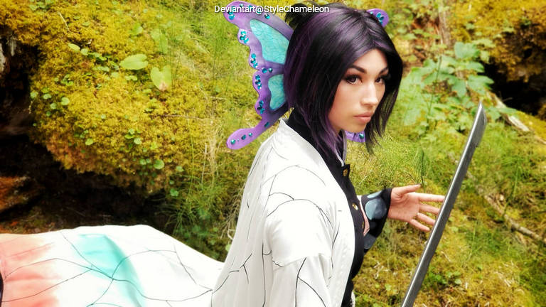 A person in a fantastical costume with butterfly wings, holding a sword, set against a natural background of moss and greenery.