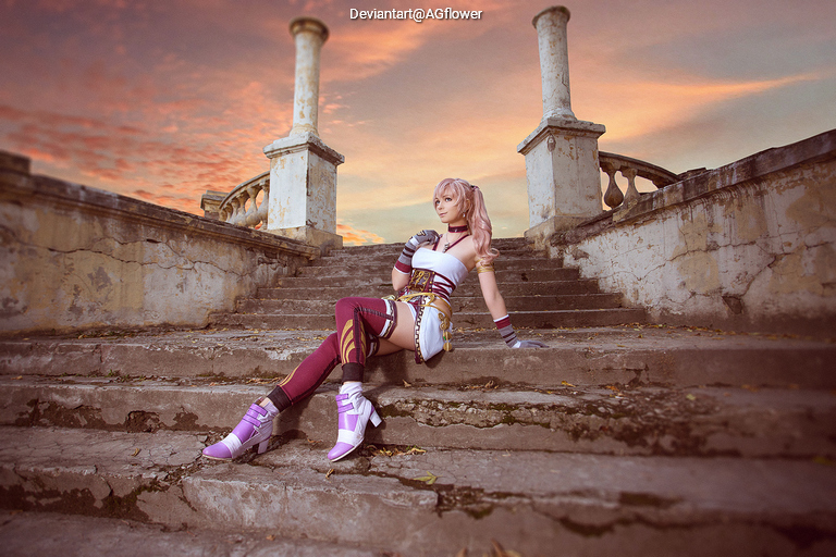 A character in a colorful costume sits on stone steps, with a scenic sunset in the background.