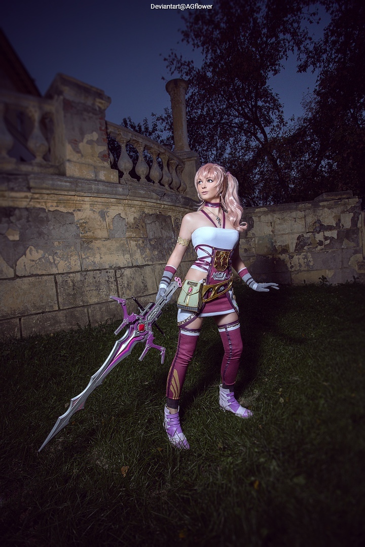 A person dressed in an elaborate fantasy cosplay outfit with a long sword, standing on grass in front of a stone wall.
