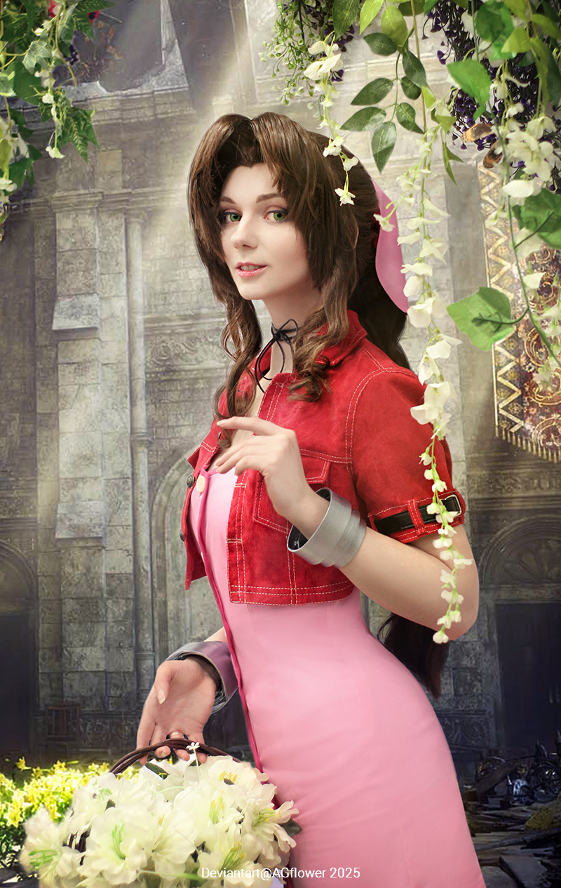 A young woman with long, wavy brown hair, wearing a pink dress with a red jacket, poses with a basket of flowers against an ornate background decorated with greenery and floral elements.