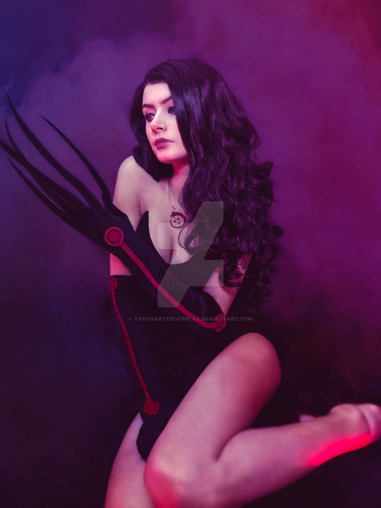 A woman with long dark hair poses against a colorful background, wearing a black outfit and an armor-style arm glove with long fingers, conveying a dramatic and artistic vibe.