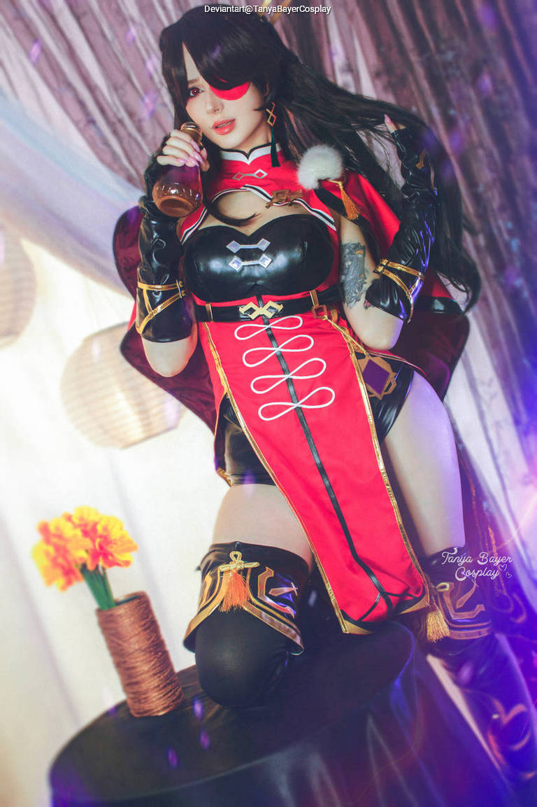 A person in a red and black cosplay outfit with an eye patch, holding a drink, seated at a table with flowers in the background.