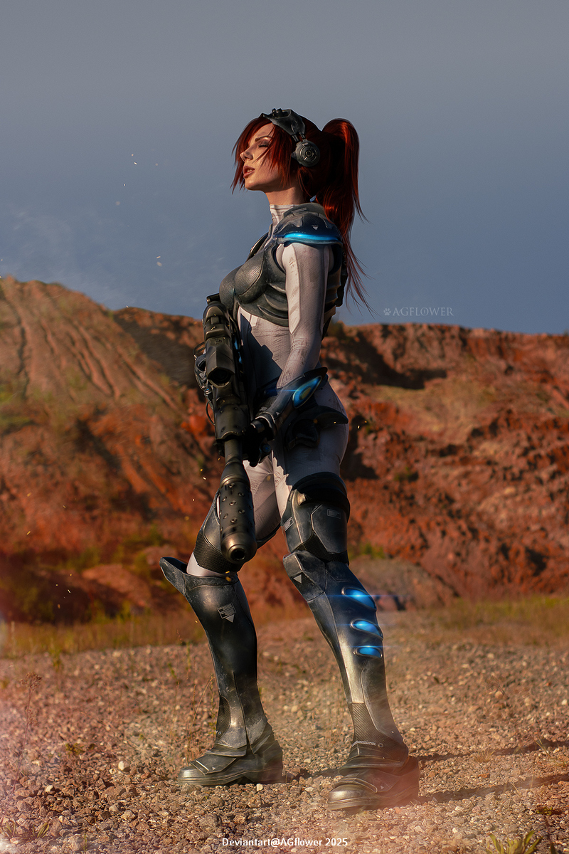 A confident female warrior in futuristic armor stands on rocky terrain, holding a weapon. She has red hair styled in a ponytail and is wearing headphones, with a intense gaze towards the horizon.