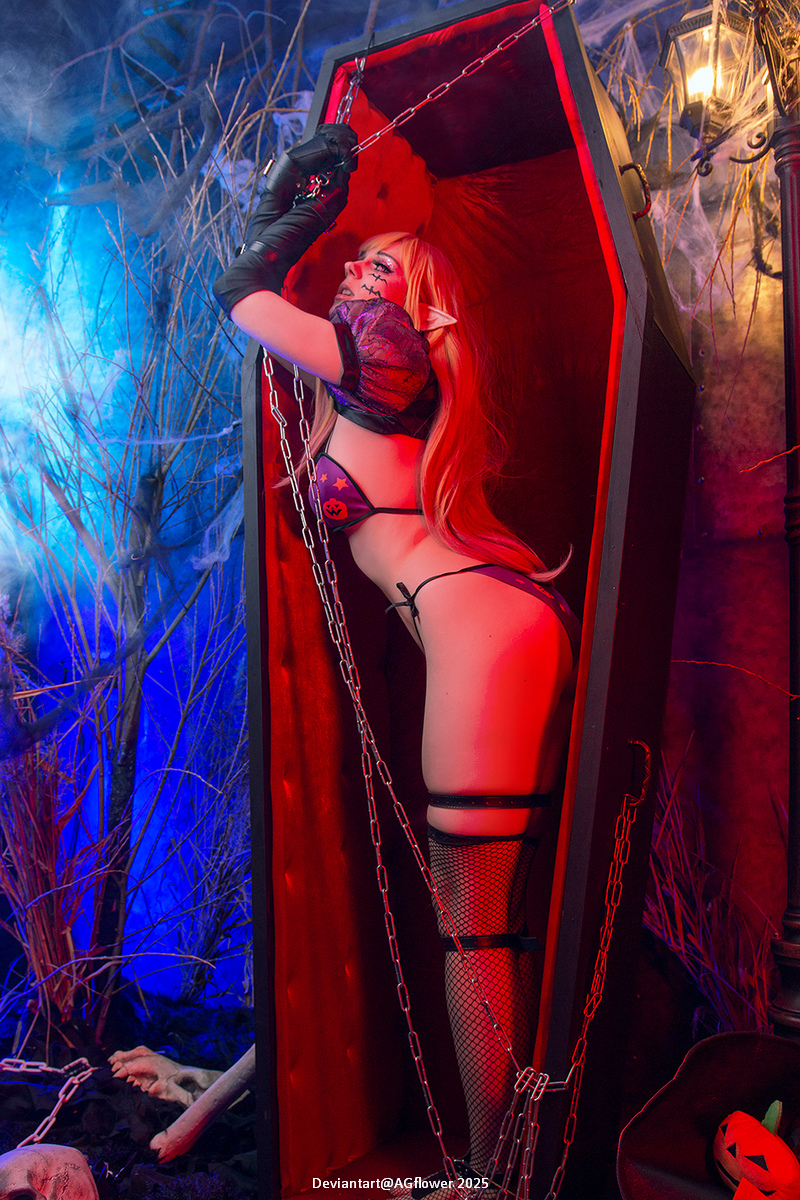 A person with long hair and pointed ears in a dark fantasy-themed setting, posing inside a red coffin, adorned with chains and dramatic lighting.
