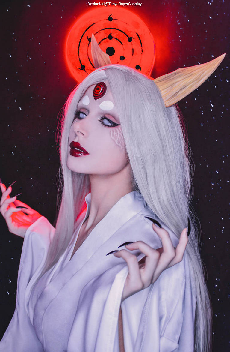 A person with long white hair and red eyes wearing a traditional white outfit, posing with a mystical red background featuring a stylized moon and black markings.
