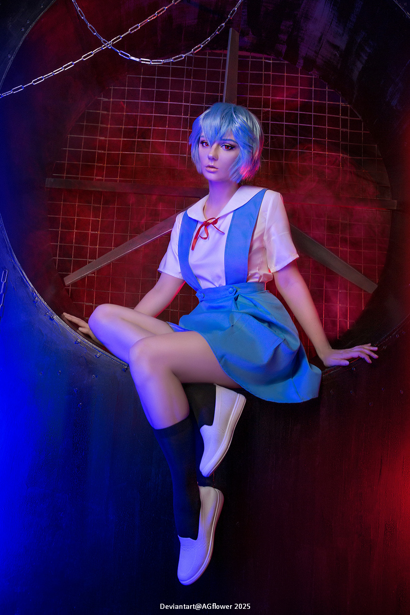 A character with short blue hair sits in a circular opening, wearing a school uniform with a blue skirt and white shirt. The background features red and blue lighting, creating a dramatic atmosphere.