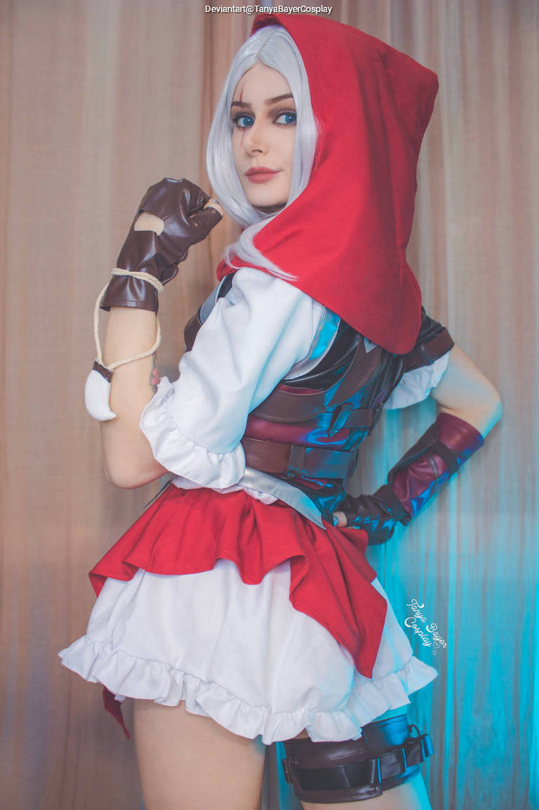 A person in a red hooded costume with a white frilled dress and dark accessories, posed with a confident expression.
