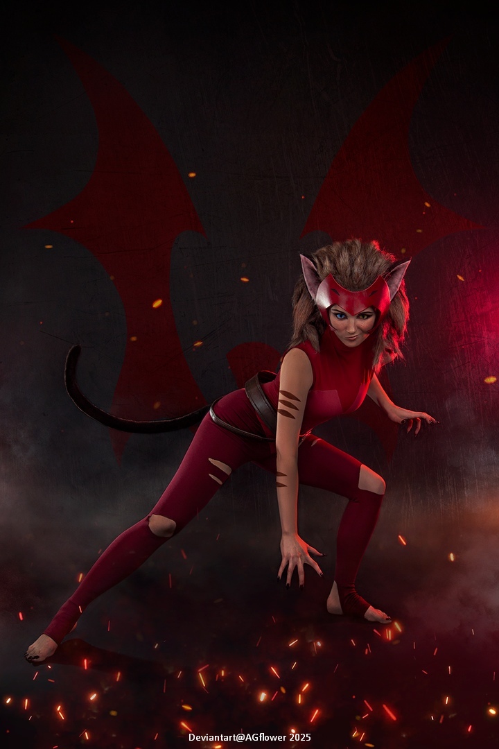 A character posed in an action stance, wearing a red outfit with cat-like features including ears and a tail, set against a dark background with glowing embers.