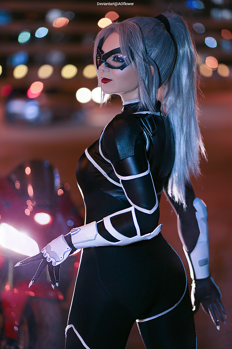 A character in a black and white costume, resembling a cat-like superhero, poses with a motorcycle in a city at night. The background features blurred lights and a dynamic urban atmosphere.