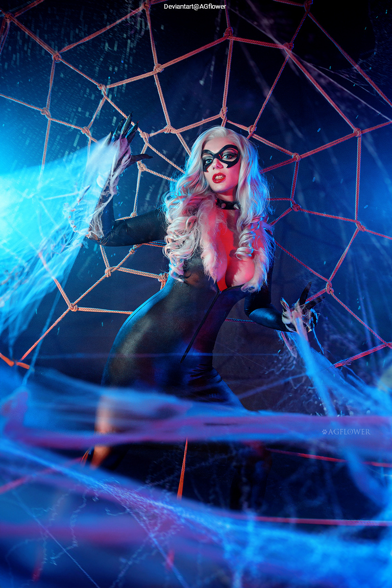 A woman dressed as a spider-themed character poses in a web-like setting with colorful lighting and fake cobwebs.