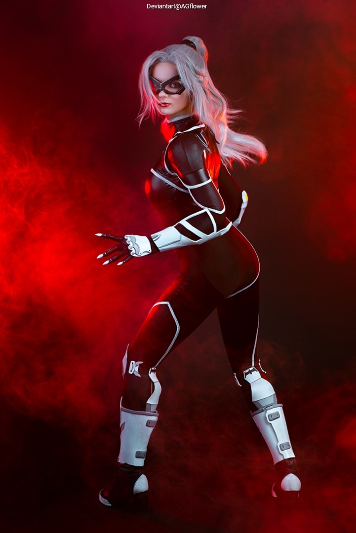 A person in a sleek black and white costume with a mask, posing dramatically against a red smoky background.