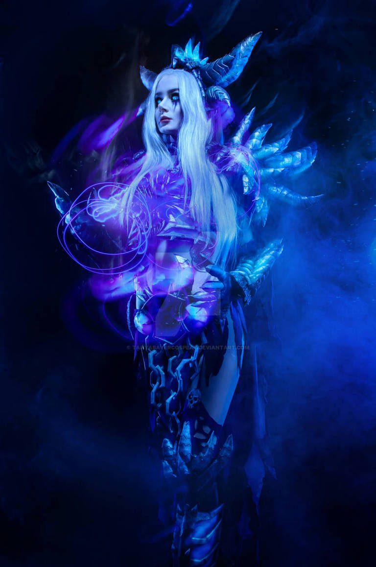A figure in an elaborate dark fantasy costume with horns and spikes, surrounded by blue and purple smoke, holding a glowing orb.